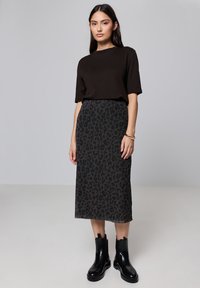 Haut noir à manches courtes associé à une longue jupe sombre à imprimé léopard, complété par des bottines noires à semelles épaisses.