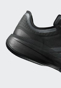 Musta urheilukenkä, jossa on teksturoitu kangaspäällinen, paksu pehmustettu pohja ja hillitty heijastava raidotus kauluksessa ja sivupaneeleissa.