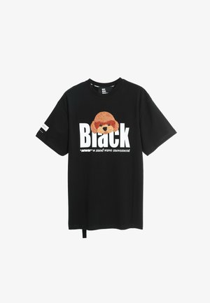 Camiseta de algodón negra que presenta un gráfico de un perro de peluche, texto en negrita "Black" y un detalle de etiqueta en la parte inferior. Manga corta y ajuste relajado.
