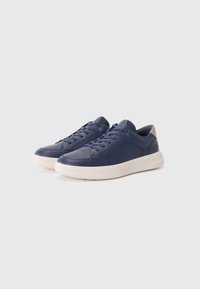 Marineblå sneakers laget av glatt materiale med hvit gummisåle, med snørebånd og en kremfarget aksent på baksiden.