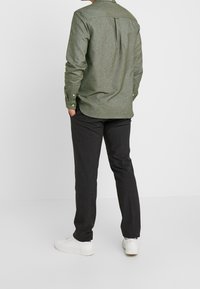 Groene overhemd met knopen, voorzien van een rugplooi, gecombineerd met zwarte broeken en witte sneakers. Het shirt heeft een kraag en lange mouwen.