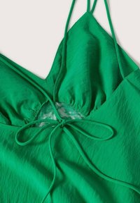 Haut licou vert avec un décolleté en V profond, tissu froncé et un panneau en dentelle au centre, doté d'une fermeture nouée à l'avant. Texture lisse.