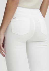 Jeggings de mezclilla blanca con cintura alta, que cuentan con bolsillos traseros y detalles de costura sutiles. Textura suave y diseño ajustado.