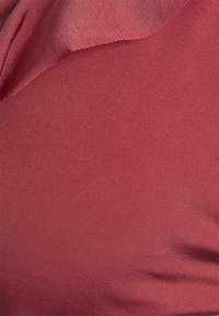 Tecido vermelho texturizado com uma superfície suave, apresentando um ligeiro brilho e variações subtis na tonalidade. Adequado para vestuário ou acessórios.