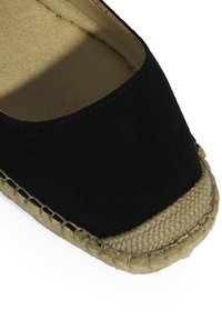 Schwarze Wildleder-Espadrille mit einer gewebten Jutesohle, die eine runde Zehenpartie und angenähte Akzente am Rand aufweist. Innenausstattung ist beige.