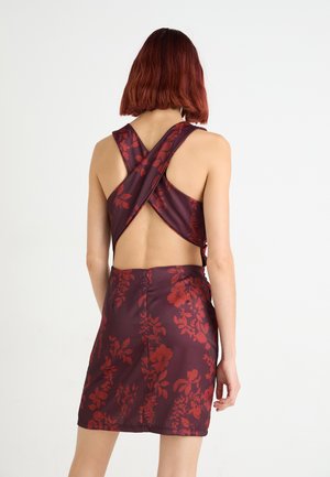 Plum dress with red floral pattern, cross-back design, and back cutout. Smooth satin texture with a fitted skirt.