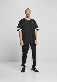 Černé oversized tričko s bílými pruhy na krátkých rukávech, kombinované s černobílými teplákovými kalhotami a černými teniskami.