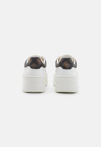 Sneakers piattaforme bianche con retro a motivo nero, caratterizzate da un tessuto testurizzato e il nome del marchio "GUESS" impresso sul tallone.