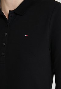 Czarna koszulka polo z teksturowanej tkaniny, z klasycznym kołnierzykiem, plisą na guziki i małym czerwono-białym logo na piersi.