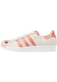 Sneakers with a beige leather upper, three rose gold stripes, a metallic rose gold toe cap, and a white rubber sole. Textured accents on the heel.