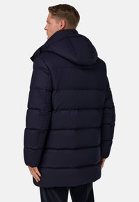 Námorně modrá zateplená bunda s kapucí, s vodorovně prošívanými sekcemi a volným střihem, vyrobena z měkké, hladké tkaniny.