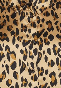 Chemise en satin imprimé léopard, avec un fond beige et des taches noires et brunes, fermeture par boutons et un col classique.