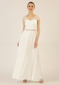 Weißes langes Kleid mit Spitzenkapellärmeln, einem figurbetonten Oberteil und einer geschichteten Spitzen-Taille. Glatte Textur, fließendes Material und A-Linie-Form.