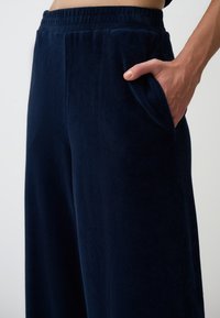 Pantalons larges en velours côtelé bleu marine avec une surface texturée, une taille élastique et des poches latérales. Tissu doux, adapté à une tenue décontractée.