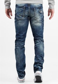 Jeans en denim bleu foncé avec une coupe slim, des détails décolorés et deux poches arrière. Associés à des baskets basses blanches et rouges.