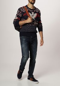 Námorníkově modrý pletený svetr s vícebarevnými vzory, modré džíny s opotřebovanými detaily a tmavé tenisky s hnědými akcenty.