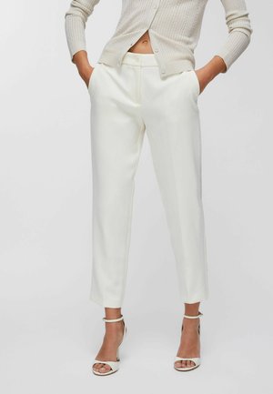 Weiße, maßgeschneiderte Hosen mit glatter Textur, gestaltet mit Seitentaschen und geradem Bein, kombiniert mit weißen Sandaletten mit Absatz.
