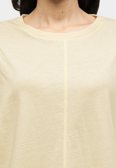 Ανοιχτό κίτρινο κοντομάνικο τοπ με στρογγυλή λαιμόκοψη, που διαθέτει λεπτή υφή και κάθετη ραφή στο κέντρο.