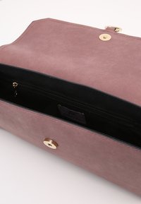 Różowa torebka z sztucznej skóry z złotym zapięciem magnetycznym, czarnym wnętrzem i dodatkową zapinaną kieszenią na przechowywanie.