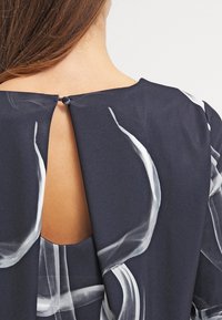 Vestido azul marino con un gran corte en la parte posterior, asegurado con un botón, adornado con patrones abstractos blancos y fabricado en tela suave y ligera.