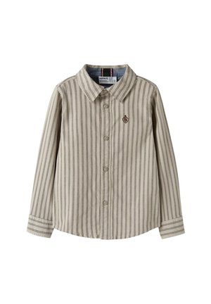 Bežina košulja s dugim rukavima i dugmadima, s tankim vertikalnim trakama i malim izvezenim grbom na lijevoj strani prsiju.