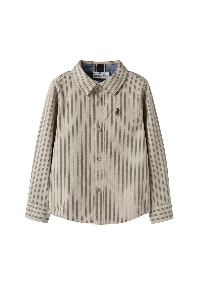 Bežina košulja s dugim rukavima i dugmadima, s tankim vertikalnim trakama i malim izvezenim grbom na lijevoj strani prsiju.