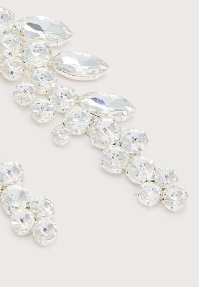 Συσσωμάτωση διαφανών επιπεδωμένων στρας σε στρογγυλά και μαρκίζ σχήματα, τοποθετημένα σε μέταλλο ασημί τόνου σε ανοιχτό φόντο.