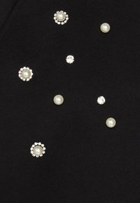 Top in tessuto nero con decorazioni sparse: perle e strass di varie dimensioni e forme, che creano un aspetto strutturato.