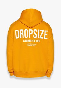 Gul hættetrøje med hvid tekst på ryggen: "DROPSIZE CRIME CLUB," "LEGENDS SINCE 2020," og "kun for medlemmer." Blødt stof, afslappet pasform.