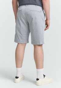 Hellgraue gemusterte Shorts mit zwei Gesäßtaschen und tailliertem Schnitt, kombiniert mit weißen Socken und beigen Sneakers.