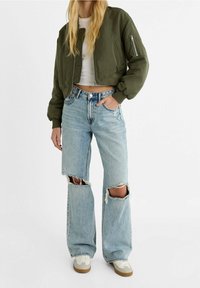 Kort bomberjack in olijfgroen, gecombineerd met lichtblauwe high-waisted jeans met grote gescheurde knieën en een losse pasvorm.