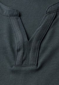 Tmavě zelená bavlněná košile má design s výstřihem do V, dvojitě šitý límec a hladkou texturu. Minimalistická a jednoduchá konstrukce.