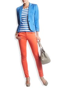 Niebieska marynarka na białej i granatowej koszuli w paski, połączona z pomarańczowymi, obcisłymi dżinsami. Szara torba i jasnoszare szpilki dopełniają strój.