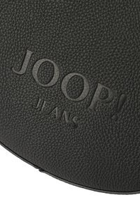Černá texturovaná kůže s embosovaným logem "JOOP! JEANS". Výrazný jemně strukturovaný povrch a hladké akcenty. Kulatý tvar, minimalistický design.