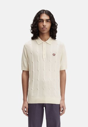 Polo de punto en color crema con un patrón de trenzas texturizadas, manga corta y un sutil logo bordado en el pecho.