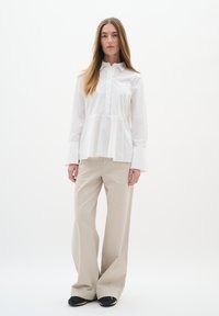 White peplum blouse with long sleeves and button front, paired with beige wide-leg trousers and black shoes with rounded toes.