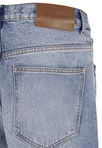 Vaqueros de mezclilla azul claro que muestran el bolsillo trasero y una etiqueta de cuero marrón con la marca "2Y Studios" en la cintura.