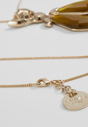 Kultainen ketjukoru, jossa on hummerilukko ja pyöreä riipus, johon on kaiverrettu "PATRIZIA PEPE" valkoisella taustalla.