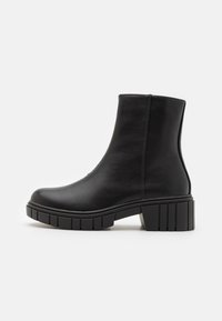 Bottines noires en cuir lisse avec un talon bloc et une semelle épaisse et crantée. Présente un design simple et sans couture, avec une fermeture éclair sur le côté.