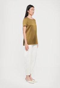 Blusa verde oliva a maniche corte con scollo rotondo abbinata a pantaloni bianchi larghi. Indossata con mules bianchi a punta.