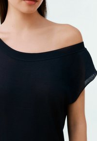 Zwarte off-the-shoulder top met een relaxte pasvorm. Kenmerkt zich door een geribbelde halslijn en een zachte, gladde stof. Naadloze randen en een licht doorschijnende textuur.