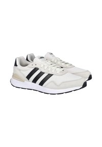 Zapatillas blancas de malla y ante, con tres rayas negras, punta redonda, diseño con cordones y una entresuela blanca con suela exterior negra.