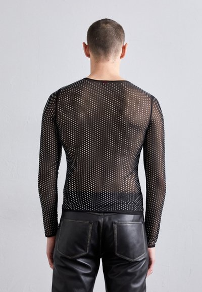 Musthave, mustade pikad varrukad võrgusilmast topp, millel on täppidega muster, ümmargune kaelus ja keha lähedane lõige, koos mustade nahkpükstega.