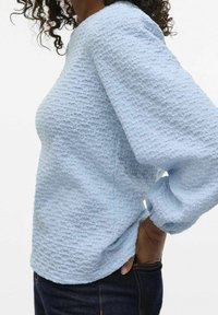 Light blue textured sweater with a round neckline and long, slightly puffed sleeves, paired with dark jeans.