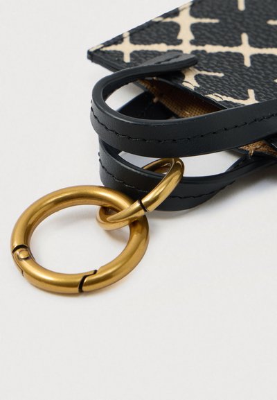 Must mustranahk rihm, mis on kinnitatud musta ja valge mustriga kangatükile, millel on kaks omavahel ühendatud kuldset metallringi valge tausta peal.