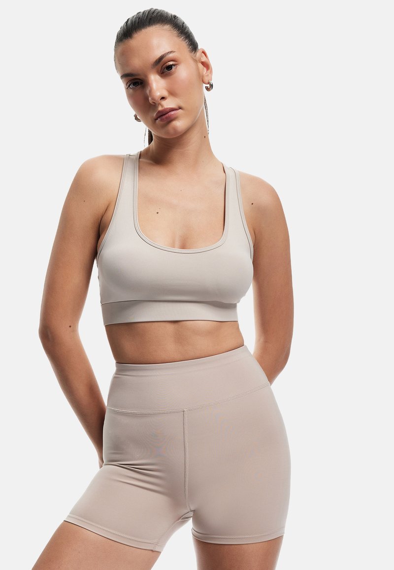 Beige sports-bh med brede stropper og firkantet halsudskæring, parret med højttaljede, matchende beige shorts med en glat tekstur.