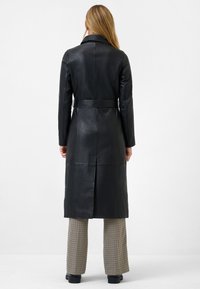 Black leather long coat with a belted waist, notched collar, and back vent, paired with checked wide-leg trousers and black boots.