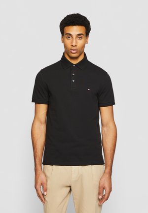 Melnā kokvilnas polo krekls ar apkakli, trīs pogu slēgšanu, īsām piedurknēm un mazu viņa zīmola logotipu.krūšu daļā.