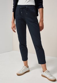 Marineblaue Jogginghosen mit einem Kordelzug-Bund, schmal zulaufenden Beinen und weichem Baumwollmischgewebe, kombiniert mit weißen Sneakers mit beigen Akzenten.