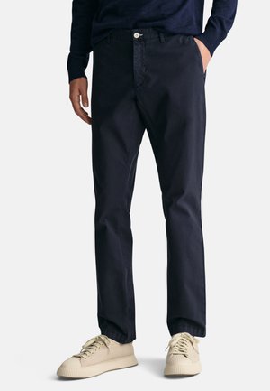 Pantalones de algodón azul marino con diseño de pierna recta, que cuentan con bolsillos frontales, un cierre de botón único y se combinan con zapatillas beige.